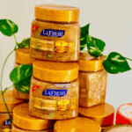 La’Fresh Gold scrub jars stacked with golden exfoliating texture, featuring deep exfoliating face and body scrub enriched with gold, collagen, and vitamin E, 500ml packaging displayed with green leaves background.