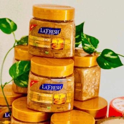 La’Fresh Gold scrub jars stacked with golden exfoliating texture, featuring deep exfoliating face and body scrub enriched with gold, collagen, and vitamin E, 500ml packaging displayed with green leaves background.