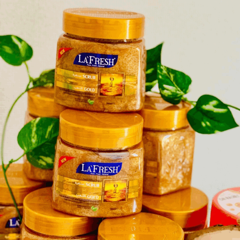 La’Fresh Gold scrub jars stacked with golden exfoliating texture, featuring deep exfoliating face and body scrub enriched with gold, collagen, and vitamin E, 500ml packaging displayed with green leaves background.