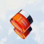 Dr. Rashel Vitamin C Brightening Face Night Cream 50g in a glossy orange jar with a reflective silver lid, photographed at an angle with a mirrored reflection on a light background, highlighting its brightening and anti-aging formula with niacinamide.