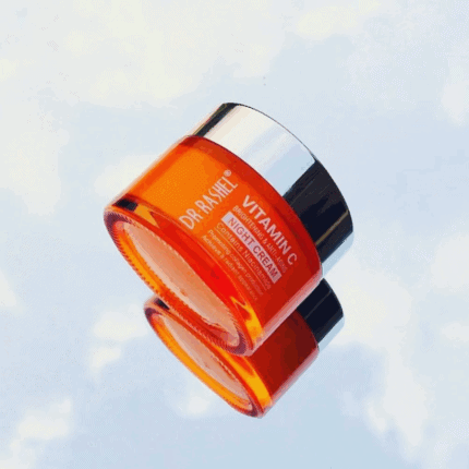 Dr. Rashel Vitamin C Brightening Face Night Cream 50g in a glossy orange jar with a reflective silver lid, photographed at an angle with a mirrored reflection on a light background, highlighting its brightening and anti-aging formula with niacinamide.