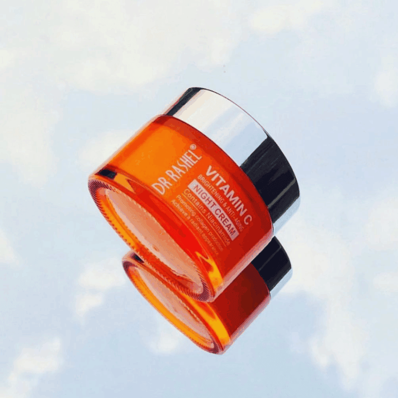 Dr. Rashel Vitamin C Brightening Face Night Cream 50g in a glossy orange jar with a reflective silver lid, photographed at an angle with a mirrored reflection on a light background, highlighting its brightening and anti-aging formula with niacinamide.
