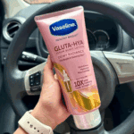 Hand holding Vaseline Healthy Bright Gluta-Hya Dewy Radiance serum burst lotion inside a car, showing the pink 330ml tube with GlutaGlow, Hyaluron, and Niacinamide on the label.