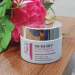 Dr Rashel Fade Spots Night Cream jar with silver lid on wooden surface beside pink flowers, formulated with arbutin and niacinamide