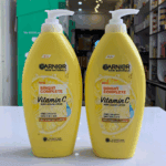 Two yellow Garnier Skin Naturals Bright Complete Vitamin C body serum lotion bottles with white pump dispensers placed side by side on a counter inside a cosmetics store, showing lemon graphic and “2X Vitamin C + Lemon” label clearly.
