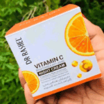 Dr. Rashel Vitamin C Brightening Night Cream box held in hand outdoors, featuring orange slice graphics on white and orange packaging, highlighting its anti-aging formula with vitamin C and niacinamide.