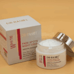 Dr Rashel Fade Spots Night Cream with open jar and packaging box on beige background, showing white cream texture with arbutin and niacinamide formula