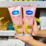 Hands holding two Vaseline Healthy Bright Gluta-Hya Dewy Radiance serum burst lotion tubes on a store shelf, showing the pink 330ml packaging with GlutaGlow, Hyaluron, and Niacinamide claims for dewy bright skin.