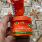 Hand holding Cantu Shea Butter Leave-In Conditioning Cream jar showing front label