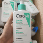 Hand holding CeraVe Foaming Cleanser 236ml bottle with pump in a storage box