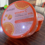 Side angle view of Dr. Rashel Vitamin C Soothing Gel 99% jar with orange packaging on wooden surface
