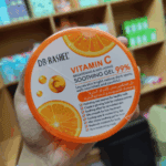 Hand holding Dr. Rashel Vitamin C Brightening Soothing Gel 99% jar inside cosmetic store shelf background