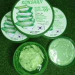 Open Roushun Aloe Vera 99% gel showing fresh green gel texture alongside closed tubs on a grass background.