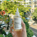 Hand holding The Ordinary Glycolic Acid 7% Exfoliating Toner bottle with outdoor city background