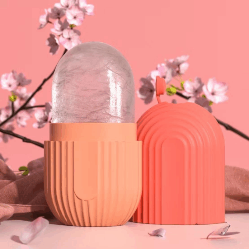 Pink silicone ice roller with capsule-shaped cover used for facial cooling and skincare, displayed with soft floral background