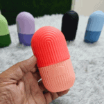 Hand holding pink silicone ice roller with ribbed grip, multiple color variants displayed in background