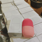 Pink silicone ice roller placed beside white retail packaging box labeled 100ml, stacked product boxes in background