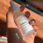 Hand holding The Ordinary Niacinamide 10% + Zinc 1% serum bottle in warm indoor lighting