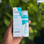 Hand holding CeraVe Resurfacing Retinol Serum bottle next to box packaging with green leaf background