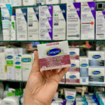 Hand holding Cetaphil Healthy Radiance Brightening Cream box in front of Cetaphil skincare products shelf