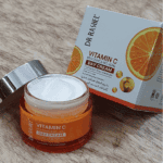 Open Dr. Rashel Vitamin C Day Cream showing texture beside original packaging with orange vitamin C design