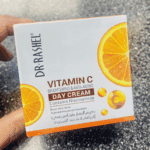 Hand holding Dr. Rashel Vitamin C Brightening & Anti-Aging Day Cream box with orange slice vitamin C visuals