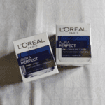 L’Oréal Paris Aura Perfect Day Cream and Night Cream boxes placed side by side on a light fabric background