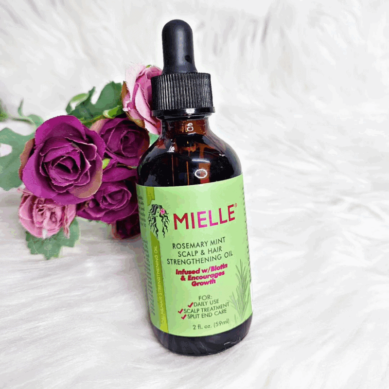Mielle Rosemary Mint Scalp and Hair Strengthening Oil bottle placed on white fur background with purple roses