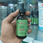 Hand holding Mielle Rosemary Mint Scalp and Hair Strengthening Oil bottle inside a retail store