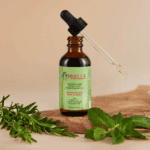 Open Mielle Rosemary Mint Scalp and Hair Strengthening Oil bottle with dropper and rosemary leaves on wooden surface