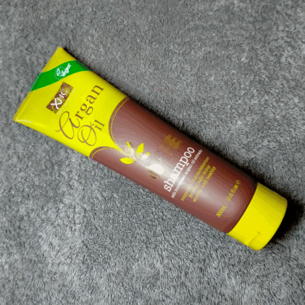 XHC Argan Oil shampoo tube placed diagonally on a grey textured fabric surface