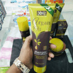 Hand holding XHC Argan Oil shampoo tube with other hair care products displayed in the background
