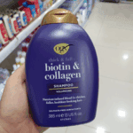 Hand holding OGX Biotin and Collagen Shampoo bottle inside a retail store aisle
