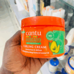 Hand holding cantu avocado hydrating curling cream jar in store setting