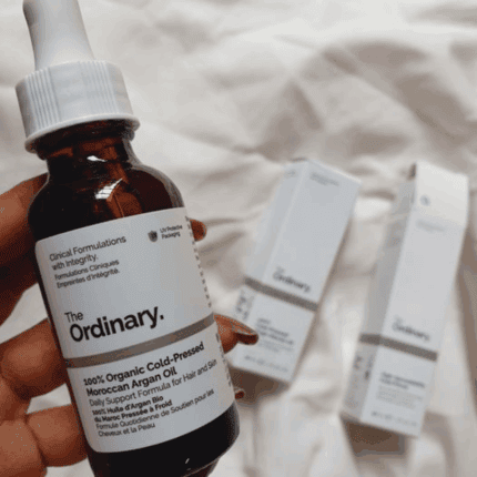 Hand holding The Ordinary 100% Organic Cold-Pressed Moroccan Argan Oil bottle with packaging in background