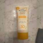 Aveeno Protect + Hydrate SPF 30 sunscreen tube placed on a marble surface, showing product label and size details.
