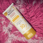 Aveeno Protect + Hydrate SPF 30 sunscreen tube lying on a pink textured fabric background.