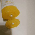 Close-up of Aveeno Protect + Hydrate SPF 30 sunscreen tube with flip cap open, showing lotion being dispensed.
