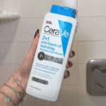 Hand holding CeraVe 2 in 1 Anti Dandruff Hydrating Shampoo 355ml in shower, with pyrithione zinc helps remove flakes and maintain healthy scalp barrier.
