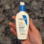 Hand holding CeraVe AM Facial Moisturizing Lotion SPF 30 bottle against a dark speckled background.