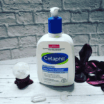 Cetaphil Daily Facial Cleanser 473ml bottle placed on wooden surface with decorative elements, fragrance free face wash for combination to oily sensitive skin with hydrating glycerin and vitamins B5 and B3.