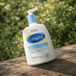 Cetaphil Gentle Skin Cleanser 500ml bottle placed outdoors on a wooden surface with green plants background, gentle soap free cleanser for sensitive skin.