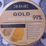 A jar of Dr. Rashel Gold Soothing Gel 99% (300g) placed on a soft patterned fabric with cartoon bear designs, showing the gold lid with product details about soothing, hydrating, and improving skin vitality.
