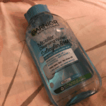 Garnier Micellar Cleansing Water with Salicylic BHA placed on fabric surface, removes makeup, cleanses and helps reduce acne and dark spots for acne prone skin.