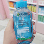 Hand holding Garnier Micellar Cleansing Water with Salicylic BHA for dull acne prone skin, removes makeup, cleanses and helps reduce acne and dark spots, store shelf background.