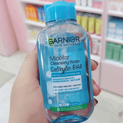 Hand holding Garnier Micellar Cleansing Water with Salicylic BHA for dull acne prone skin, removes makeup, cleanses and helps reduce acne and dark spots, store shelf background.