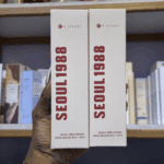 Hand holding two K-Secret Seoul 1988 Cream Snail Mucin 93% + Rice 100ml box packages in a skincare store.