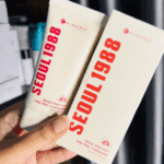 Hand holding K-Secret Seoul 1988 Sun Pine Tree + Ceramide SPF50+ sunscreen 50ml tube and box packaging in a cosmetics store.