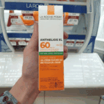 Hand holding a boxed La Roche-Posay Anthelios XL SPF 60 sunscreen in a store aisle with price tags visible in the background.