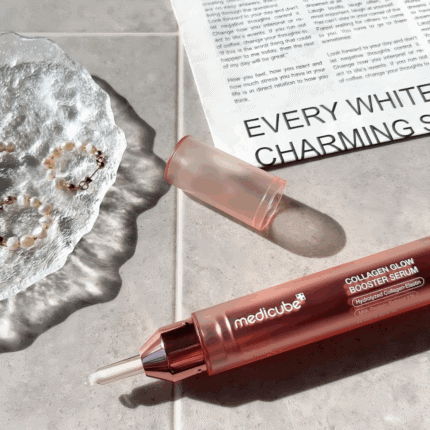 Medicube Collagen Glow Booster Serum 15ml bottle with applicator tip placed on a tiled surface next to jewelry and a magazine.